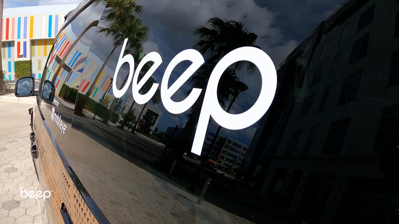 A Beep-branded vehicle with buildings and palm trees reflected in its windows.
