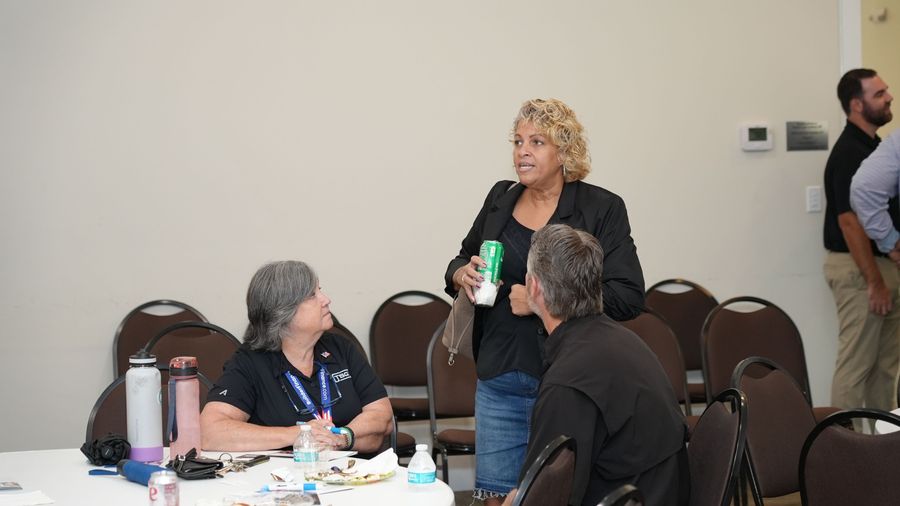 A standing attendee chats with two people seated at an event table.