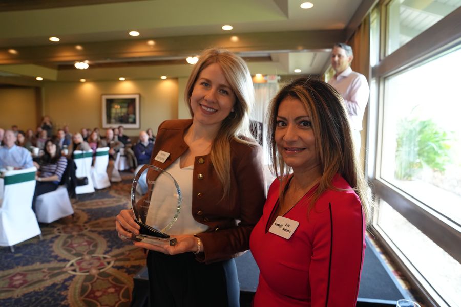 Two guests smiling with an award beside the event tables.