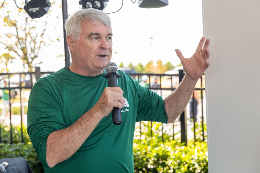 A man in a green HomeAid shirt speaks into a microphone at the tournament.