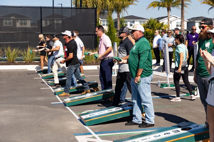 Players line up along a row of cornhole boards at the outdoor tournament.