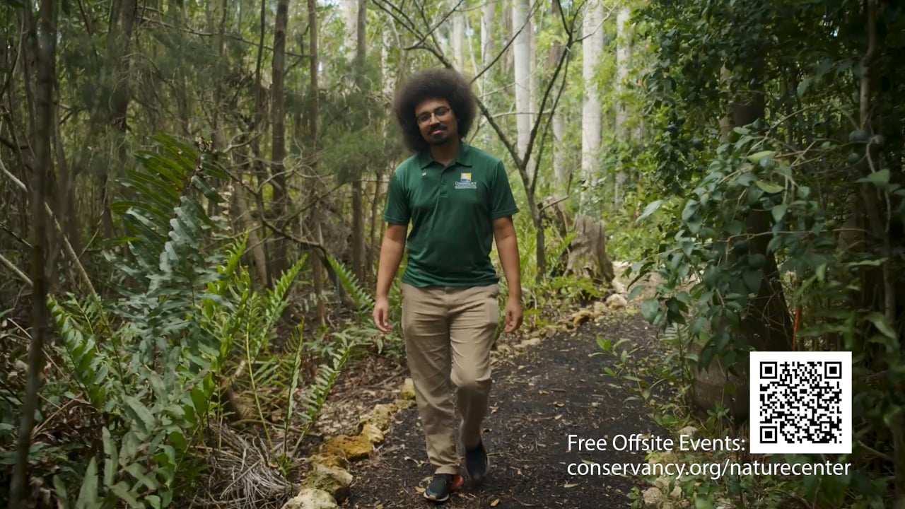A Conservancy team member walking through a wooded trail, with a nature-center web address on screen.