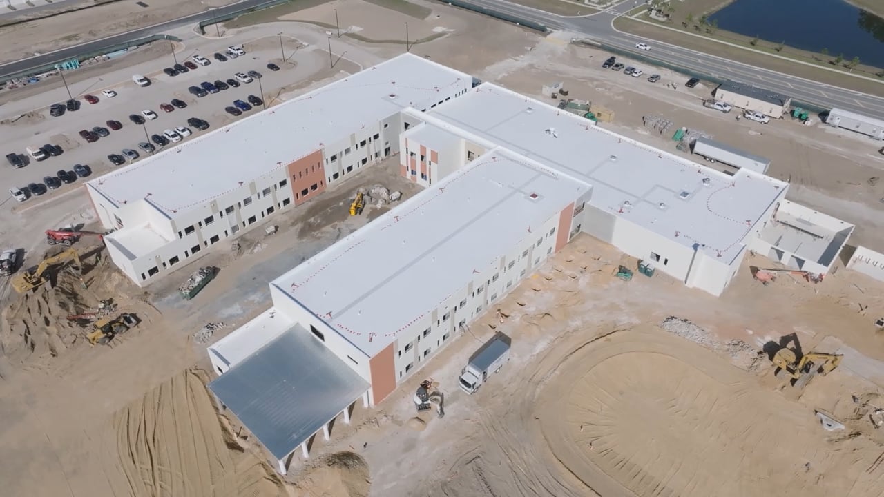 Aerial view of a school building under construction, with site vehicles and access roads.