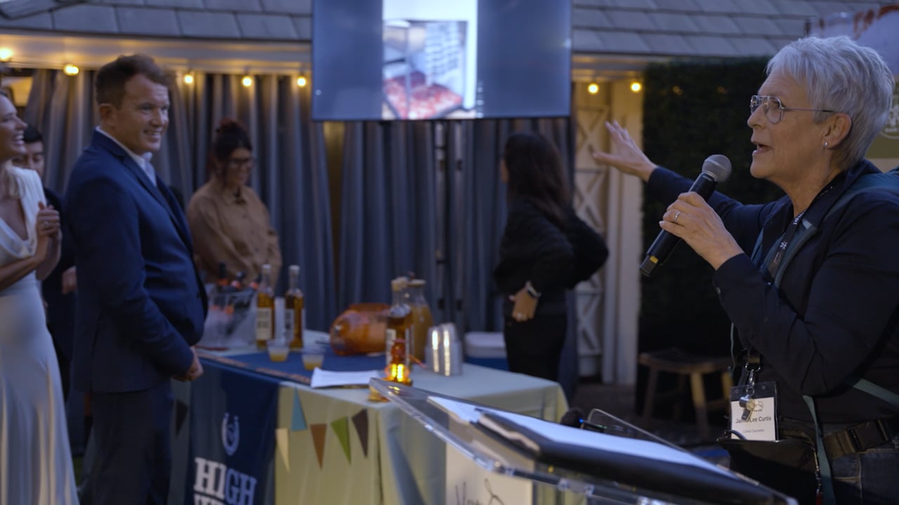 A speaker holding a microphone addresses guests at an outdoor event.