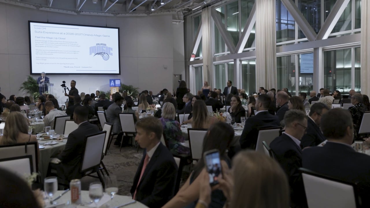 Guests seated at tables during a gala auction, with an event presentation on a large screen.
