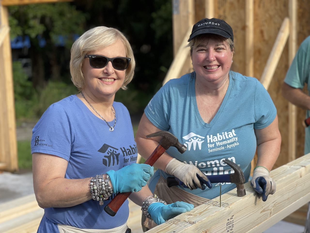Two Habitat for Humanity Women Build volunteers holding hammers at a building site