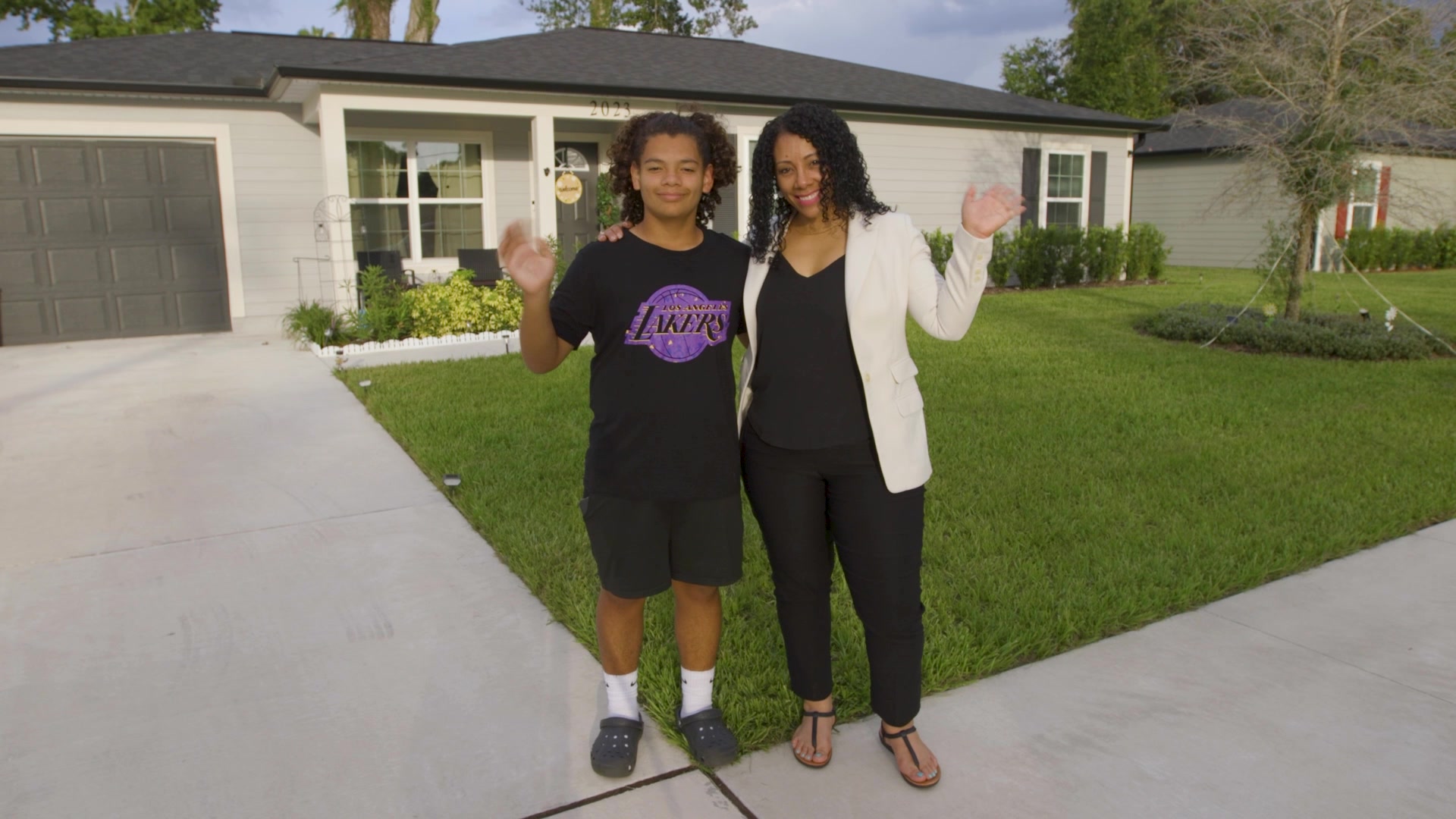 Jacqueline Pacheco and a young person waving outside a house
